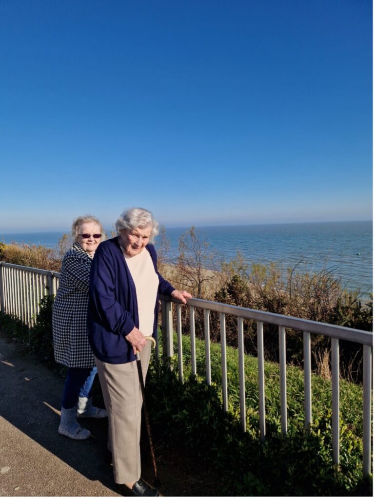 two female residents standing by a green railing with the beach in the background